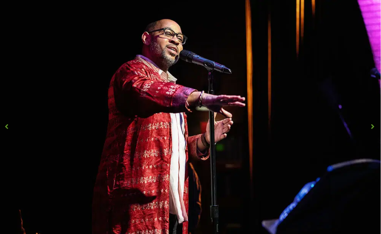 Mo Beasley performing at the microphone in a red embroidered robe