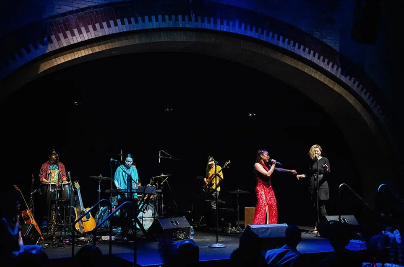 Two vocalists and full band performing under a blue-lit arch