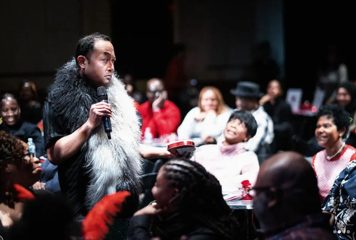 Performer in a fur wrap speaking into a microphone among the audience